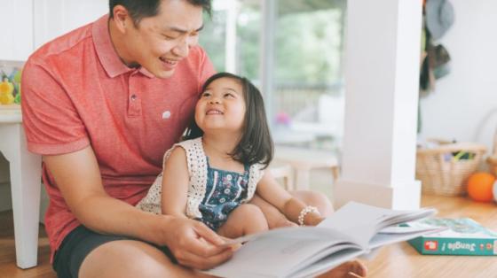 Man reading to a young girl sitting in his lap