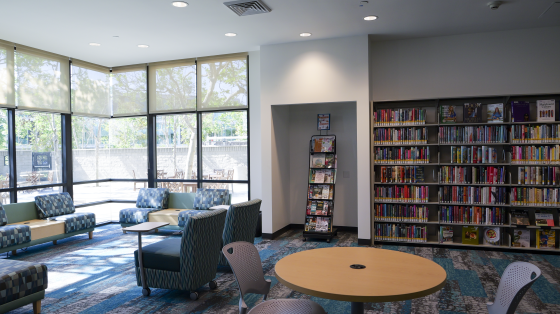 Photo of library interior with chairs placed near window, books on shelves, and table with two chairs around.